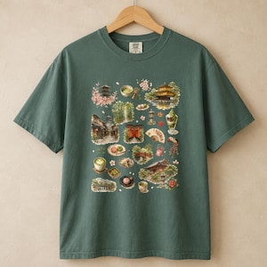 以下が含まれることがあります： ダークセージグリーンの半袖Tシャツ。中央には、五重塔、桜、抹茶、伝統的な建築物、赤い鳥居、扇子など、日本をテーマにした様々なイラストがグラフィックプリントとして描かれています。