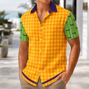 May include: A short-sleeve button-down shirt featuring a yellow and orange gingham pattern on the main body, green sleeves with a repeating black bat print, a solid purple collar, and a horizontal purple stripe along the bottom hemline.