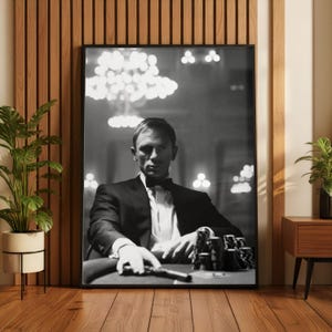 May include: Black and white framed print of a man in a tuxedo, seated at a poker table. The image features a man with a serious expression, a gun, and poker chips. The background includes soft lighting.