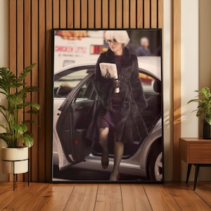 May include: A framed print showing a woman stepping out of a car. She is dressed in a dark fur coat, a purple dress, and sunglasses, holding a magazine. The car door is open, with a city street visible in the background.