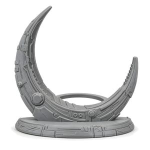 May include: A grey crescent-shaped sculpture featuring intricate mechanical and geometric surface detailing. The object is mounted on a circular base with matching panel-like textures, creating a structured, technical appearance throughout the piece.