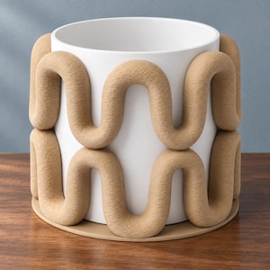 May include: A cylindrical white planter featuring a textured, tan-coloured wavy trim that wraps around the exterior in two stacked rows. The planter sits on a flat, circular tan base, creating a contrast between the smooth white surface and the tan.