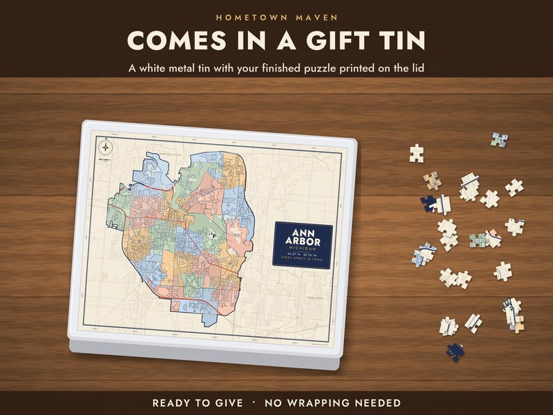 Op de afbeelding: Een witte metalen geschenkblik met een kaart van Ann Arbor, Michigan, op het deksel gedrukt. De tekst luidt HOMETOWN MAVEN, COMES IN A GIFT TIN, A white metal tin with your finished puzzle printed on the lid, ANN ARBOR MICHIGAN, READY TO GIVE, NO WRAPPING NEEDED.