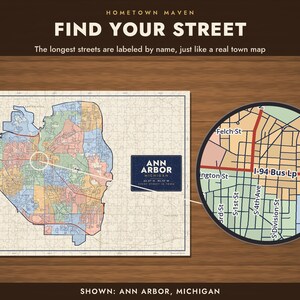 Op de afbeelding: Een legpuzzel met een kaart van Ann Arbor, Michigan, met de tekst "HOMETOWN MAVEN FIND YOUR STREET" en "ANN ARBOR MICHIGAN". De puzzel toont een kleurrijk stadsraster met gelabelde straten en een cirkelvormig vergrootglaseffect.