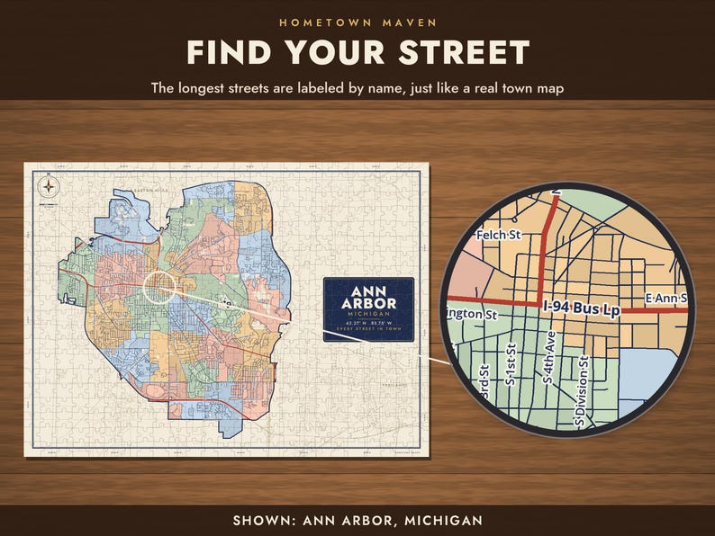 Op de afbeelding: Een legpuzzel met een kaart van Ann Arbor, Michigan, met de tekst "HOMETOWN MAVEN FIND YOUR STREET" en "ANN ARBOR MICHIGAN". De puzzel toont een kleurrijk stadsraster met gelabelde straten en een cirkelvormig vergrootglaseffect.