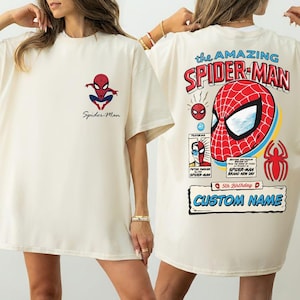 K&ouml;nnte beinhalten: Cremefarbenes T-Shirt mit einem Spider-Man-Motiv auf der Vorder- und R&uuml;ckseite. Die Vorderseite hat ein kleines Spider-Man-Logo und die Worte "Spider-Man". Die R&uuml;ckseite zeigt ein gro&szlig;es Spider-Man-Maskendesign mit dem Text "the AMAZING SPIDER-MAN."