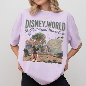 Puede incluir: Camiseta lila claro con un gr&aacute;fico de Disney World. El gr&aacute;fico incluye el texto "DISNEY WORLD The Most Magical Place on Earth" sobre una ilustraci&oacute;n de Mickey Mouse, un castillo y otros puntos de referencia del parque.