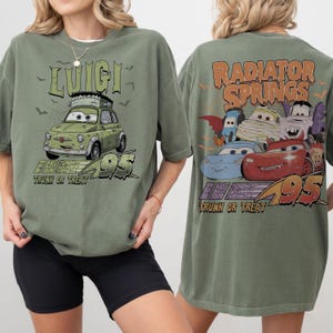 May include: An olive green t-shirt with a cartoon car design, the name "Luigi", and the text "Trunk or Treat 95" on the front. The back of the shirt shows "Radiator Springs" and Halloween-themed car characters.