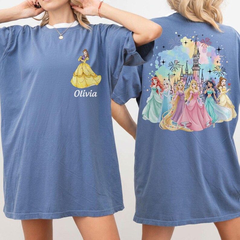 May include: Blue t-shirt featuring a princess graphic on the front and back. The front displays a yellow gown and the name "Olivia". The back showcases a castle and several princesses in colorful gowns.