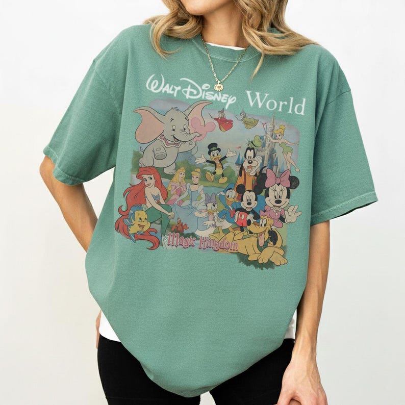 Puede incluir: Una camiseta de manga corta color verde salvia con un estampado gr&aacute;fico de varios personajes de Disney, incluidos Dumbo, Ariel, Cenicienta, el Pato Donald, Goofy, Mickey Mouse, Minnie Mouse y Pluto, con el texto Walt Disney World Magic Kingdom.