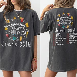 May include: Dark grey t-shirt with the text "Drinking Around the World" and "Jason's 30th!" in white. The front design features drink illustrations. The back lists countries with check boxes.
