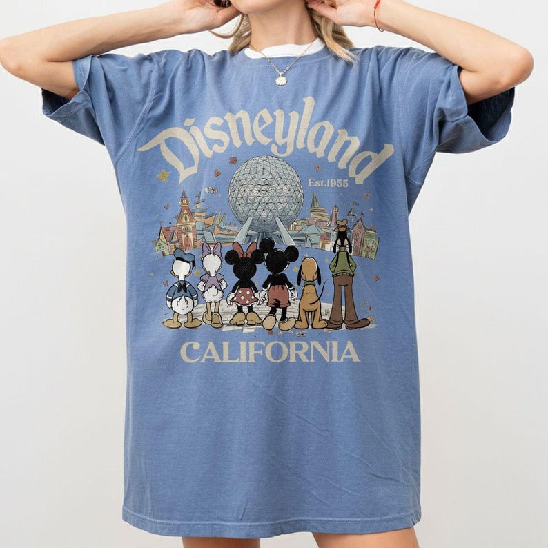 May include: A blue t-shirt with a Disneyland graphic. The graphic features the Disneyland logo, the text "Est.1955", and illustrations of Disney characters and landmarks. The word "CALIFORNIA" is printed at the bottom.