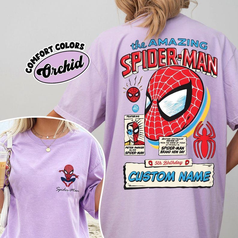 K&ouml;nnte beinhalten: Ein helllila T-Shirt mit dem Text "the AMAZING SPIDER-MAN" und einer Grafik von Spider-Mans Maske. Das Shirt hat auch den Text "COMFORT COLORS Orchid" und "CUSTOM NAME". Ein kleineres Spider-Man-Motiv befindet sich auf der Vorderseite.
