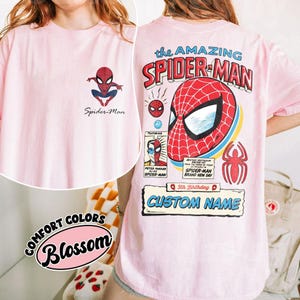 K&ouml;nnte beinhalten: Hellrosa T-Shirt mit Spider-Man-Motiven. Auf der Vorderseite befindet sich ein kleines Spider-Man-Logo und Text. Die R&uuml;ckseite zeigt ein gro&szlig;es Spider-Man-Maskendesign mit dem Text "the AMAZING SPIDER-MAN" und "CUSTOM NAME".