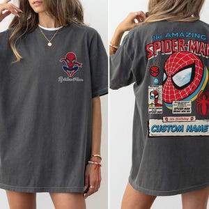 K&ouml;nnte beinhalten: Dunkelgraues T-Shirt mit Spider-Man-Grafiken auf der Vorder- und R&uuml;ckseite. Die Vorderseite zeigt ein kleines Spider-Man-Logo, w&auml;hrend die R&uuml;ckseite ein gro&szlig;es Spider-Man-Maskendesign mit dem Text "the AMAZING SPIDER-MAN" und "CUSTOM NAME" zeigt.