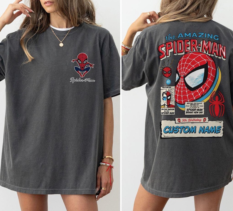 K&ouml;nnte beinhalten: Dunkelgraues T-Shirt mit Spider-Man-Grafiken auf der Vorder- und R&uuml;ckseite. Die Vorderseite zeigt ein kleines Spider-Man-Logo, w&auml;hrend die R&uuml;ckseite ein gro&szlig;es Spider-Man-Maskendesign mit dem Text "the AMAZING SPIDER-MAN" und "CUSTOM NAME" zeigt.