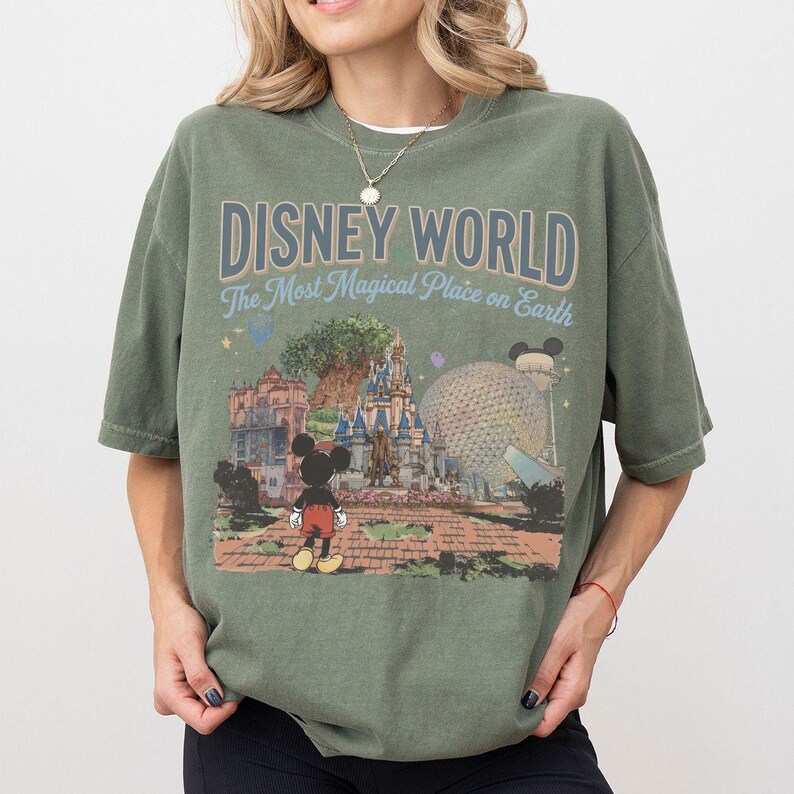 Puede incluir: Camiseta verde oliva con un gr&aacute;fico vintage de Disney World. El dise&ntilde;o presenta el texto "DISNEY WORLD The Most Magical Place on Earth" sobre una ilustraci&oacute;n del parque, incluyendo a Mickey Mouse, un castillo y Spaceship Earth.