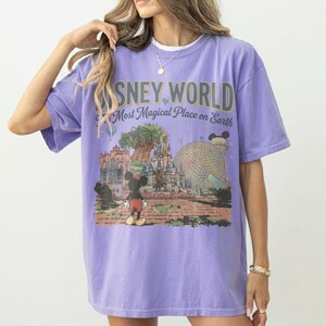 Puede incluir: Una camiseta de color lila con un gr&aacute;fico de Disney World con Mickey Mouse. El texto de la camiseta dice "Disney World, Most Magical Place on Earth". El dise&ntilde;o incluye ilustraciones del &Aacute;rbol de la Vida, el castillo de Cenicienta y Spaceship Earth.