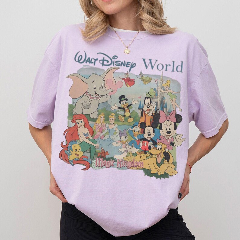 Puede incluir: Una camiseta de manga corta de color morado claro con un estampado gr&aacute;fico de varios personajes de Disney, incluidos Dumbo, Ariel, Cenicienta, Mickey Mouse, Minnie Mouse y el Pato Donald, con el texto Walt Disney World y Magic Kingdom.