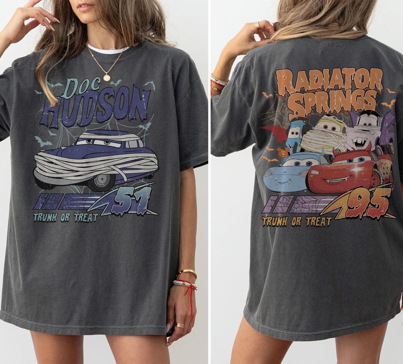 May include: Dark grey t-shirt with a graphic of Doc Hudson as a mummy, text reads "Doc Hudson 51 Trunk or Treat." The back shows "Radiator Springs 95 Trunk or Treat" with cartoon car characters in a Halloween theme.