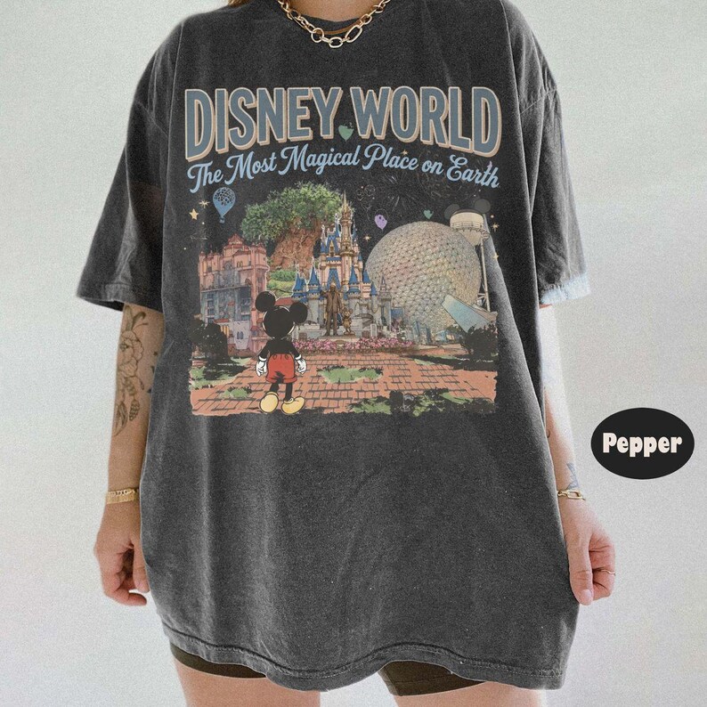 Puede incluir: Camiseta gris oscuro con un estampado colorido de Disney World con Mickey Mouse. El texto "DISNEY WORLD The Most Magical Place on Earth" est&aacute; impreso encima. La camiseta tiene mangas cortas y un corte holgado.
