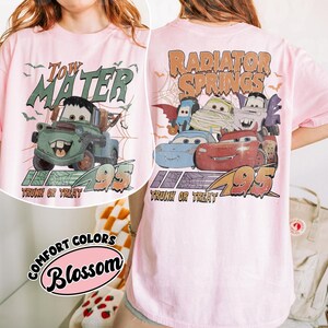 May include: Pale pink t-shirt with a Halloween-themed graphic of the character Tow Mater from the movie Cars, with the text "Tow Mater" and "Trunk or Treat 95". The back of the shirt displays "Radiator Springs" and other Cars characters.