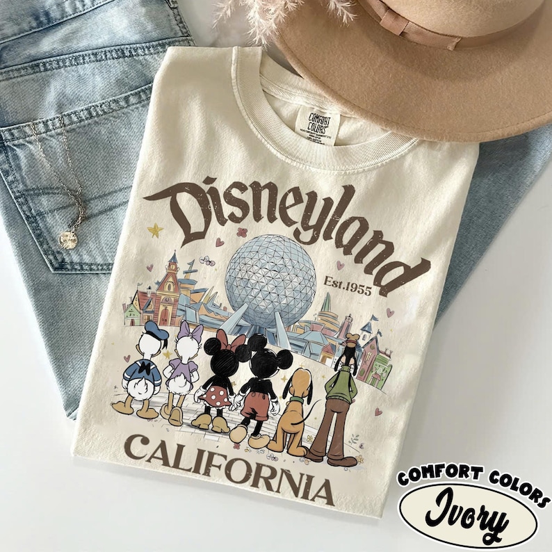 May include: Ivory-colored Disneyland California t-shirt with a graphic featuring Mickey Mouse, Minnie Mouse, Donald Duck, and Pluto. The shirt has a vintage-style design with the words "Disneyland" and "Est. 1955" in brown lettering.