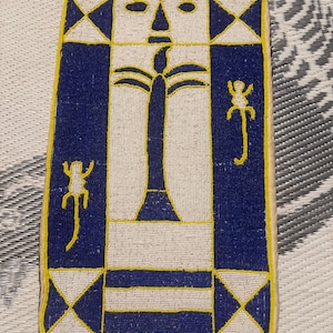 May include: Rectangular beaded artwork with a central design featuring a stylized tree and face, surrounded by blue and white geometric patterns. The artwork is framed with yellow beads and includes two monkey-like figures.