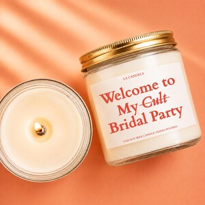 a candle labeled "Welcome to My-Gult Bridal Party" next to a glass jar with a gold-colored lid, both placed on an orange background.