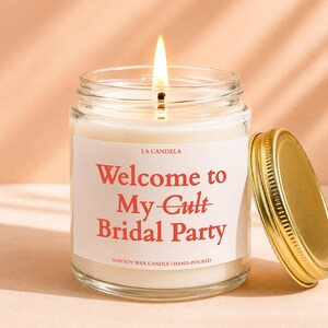 A lit candle in a glass jar with a label that says "Welcome to My Cult Bridal Party" and "100% Soy Wax Candle Hand-Poured".