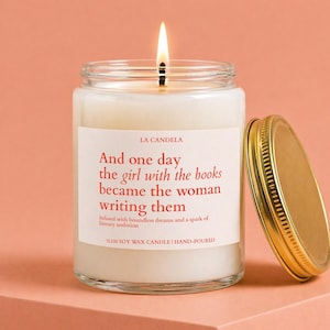 May include: A lit soy wax candle in a clear glass jar with a gold metal lid. The white label features the text: LA CANDELA, And one day the girl with the books became the woman writing them, Infused with boundless dreams and a spark of literary ambition, %100 SOY WAX CANDLE | HAND-POURED.