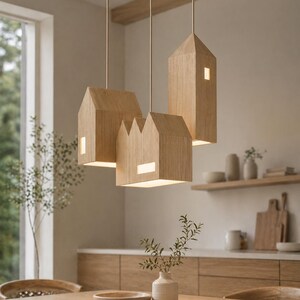 Puede incluir: Tres l&aacute;mparas colgantes de madera con forma de casa cuelgan del techo. Cada l&aacute;mpara tiene una ventana rectangular que emite un brillo c&aacute;lido. Las l&aacute;mparas est&aacute;n suspendidas sobre una mesa de comedor de madera.