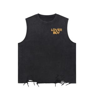 Può includere: Canotta nera con dettagli strappati e la scritta "LOVER BOY" in lettere dorate. La maglietta ha un aspetto vintage e usurato, con girocollo e bordi grezzi sul fondo.