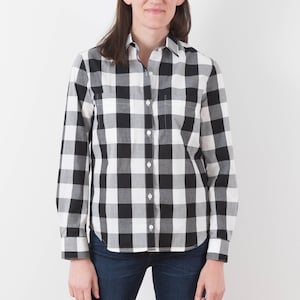 May include: A woman wearing a black and white plaid button-down shirt with long sleeves and blue jeans.