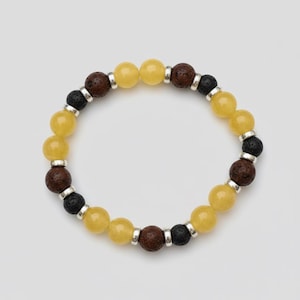 May include: A beaded bracelet featuring yellow, brown, and black stones. The bracelet has yellow, round beads, interspersed with brown and black lava beads. Silver-colored metal spacers separate the beads. The bracelet is on a white background.