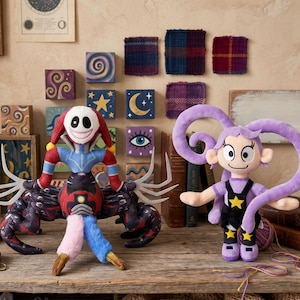 May include: A plush toy featuring a white-faced jester with red and blue limbs and dark, multi-legged spider-like appendages, standing beside a second plush toy with long purple hair, wearing black overalls adorned with yellow stars.