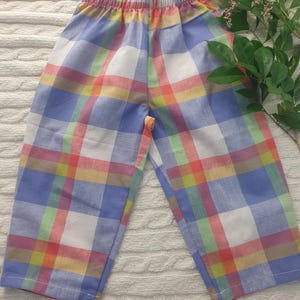 May include: A pair of trousers featuring an elasticated waistband and a multi-coloured plaid pattern. The fabric displays a grid design with intersecting lines in shades of blue, white, yellow, green, and red, creating a consistent checkered appearance.