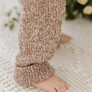 Puede incluir: Una taza de cerámica blanca con asa negra y el texto "But First, Coffee" en negrita negra. La taza se encuentra sobre un fondo borroso, sugiriendo un ambiente acogedor.