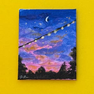 May include: Small, square painting depicting a night sky scene. The sky transitions from deep blue to pink and orange hues, with a crescent moon and string lights. Silhouetted trees are at the bottom. The painting is on a small canvas.