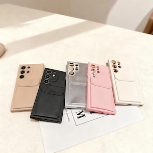 Puede incluir: Cinco fundas para teléfonos móviles en beige, negro, plateado, rosa y blanco. Cada funda tiene forma rectangular con un bolsillo para tarjetas. Las fundas se muestran sobre una superficie blanca.