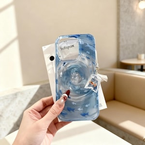 May include: Clear blue phone case with a swirling water design and small blue fish. The case has the word "Instagram" printed on it. A small charm with a miniature fish in a bag is attached to the case.