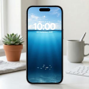 May include: A smartphone displays a serene underwater scene with a blue ocean and small fish. The screen shows the time as 10:00 AM on Monday, September 4th, 2026. A succulent plant in a terracotta pot and a white mug are visible in the background.