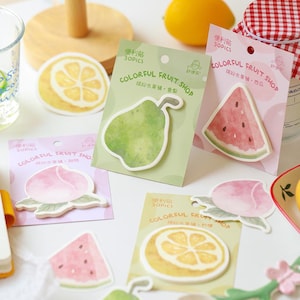 Könnte beinhalten: Eine Sammlung von bunten, fruchtförmigen Haftnotizen. Die Notizen zeigen Aquarellillustrationen einer Birne, Wassermelone, Pfirsich und Zitrone. Jede Notiz befindet sich auf einer Karte mit dem Text "COLORFUL FRUIT SHOP".