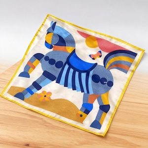 May include: A square silk scarf with a colorful geometric horse design. The horse is primarily blue with orange and yellow accents, set against a cream background with a yellow border. A butterfly and flower are also featured.