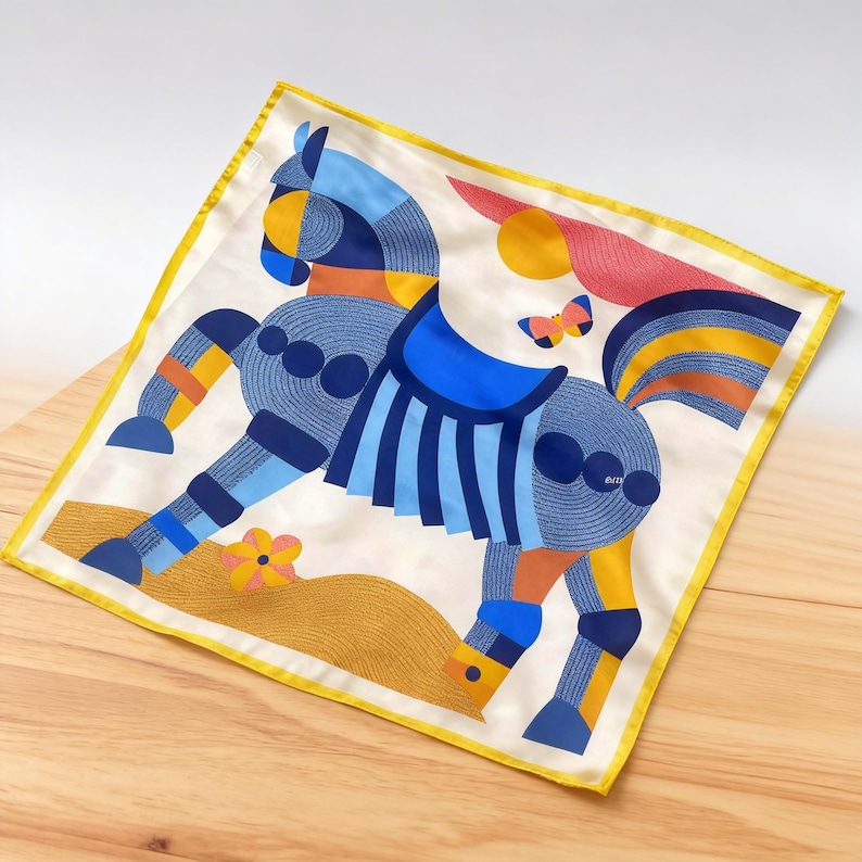 May include: A square silk scarf with a colorful geometric horse design. The horse is primarily blue with orange and yellow accents, set against a cream background with a yellow border. A butterfly and flower are also featured.
