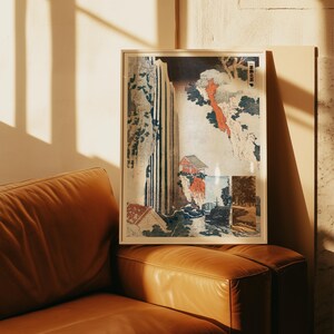May include: A framed vertical art print featuring a Japanese woodblock style landscape with a tall waterfall, a small red-roofed building on a cliff, and dark green trees. The artwork includes vertical Japanese text in the upper right corner.