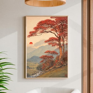May include: A framed landscape art print featuring a serene mountain scene with a river, trees, and a setting sun. The trees have vibrant red foliage, contrasting with the cool blue and green tones of the mountains and valley.