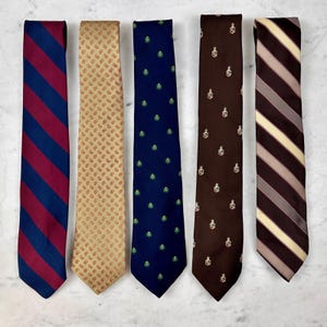 Puede incluir: Cinco corbatas con varios patrones y colores. Las corbatas incluyen una corbata a rayas azul marino y burdeos, una corbata color beige con estampado de cachemir, una corbata azul marino con diseños de árboles verdes, una corbata marrón con un escudo y una corbata a rayas marrón y beige.