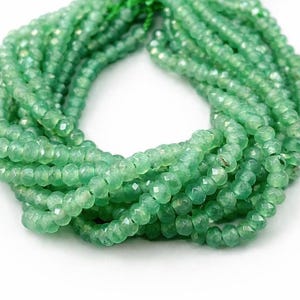 Peut inclure: Plusieurs brins de perles de pierres précieuses vert clair facettées. Les perles ont un aspect légèrement translucide et sont enfilées ensemble, créant un aspect texturé et organique. Les perles sont de couleur vert clair.