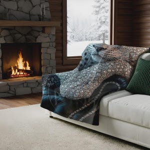 May include: A cozy white sofa with a blanket draped over it. The blanket features a detailed image of a leopard's face and a pattern of sparkling diamonds. A green pillow rests on the sofa.